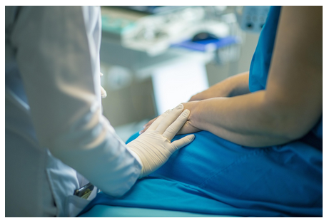 Um profissional da saúde usando luvas apoia sua mão em um braço de um paciente usando roupas hospitalares