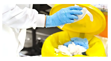 Uma enfermeira usando um jaleco e luvas descarta resíduos em um lixo amarelo