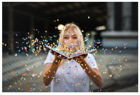 A young woman blows confetti off a book