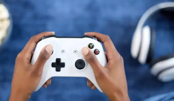 Um aparelho de videogame na mão de uma pessoa e fone de ouvido no chão
